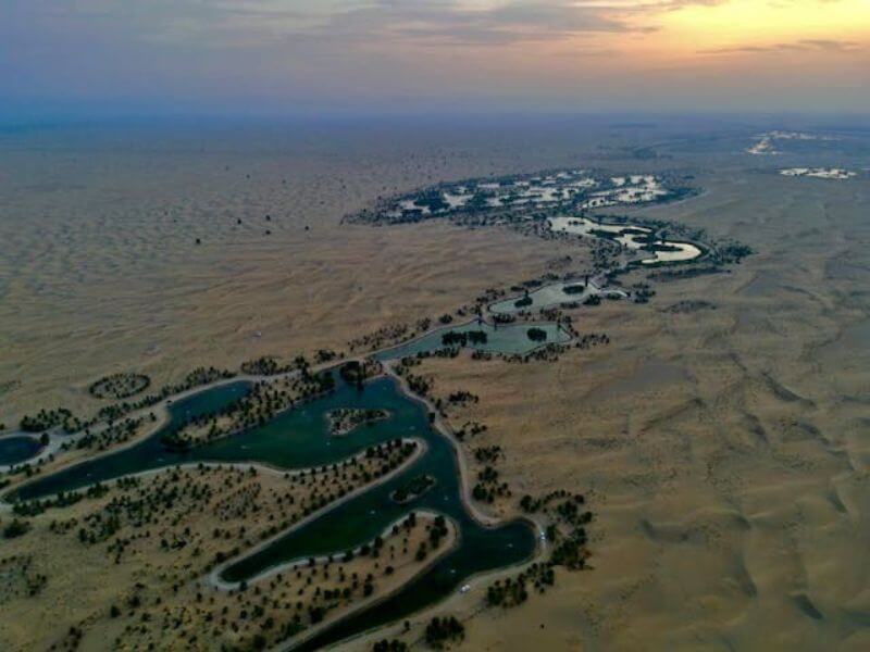 Al Qudra Lakes, Dubai Aerial view of Al Qudra Lakes in Dubai with green water lakes surrounded by trees and desert landscape at sunset.
