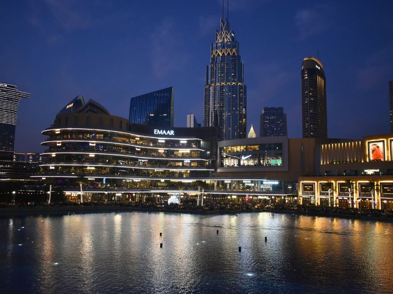 Crowds of people in front of the Dubai Mall at night Dubai Mall and surrounding buildings lit up at night with Burj Lake in the foreground reflecting the lights.