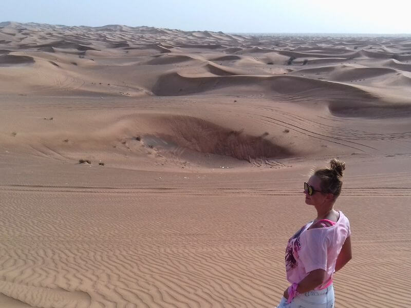 Dubai desert Woman standing in the Dubai desert with rolling sand dunes and tire tracks stretching across the landscape.