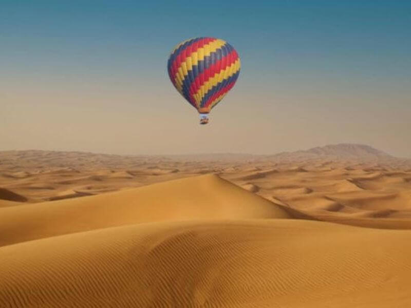 Colorful hot air balloon floating over golden sand dunes in the Dubai desert.