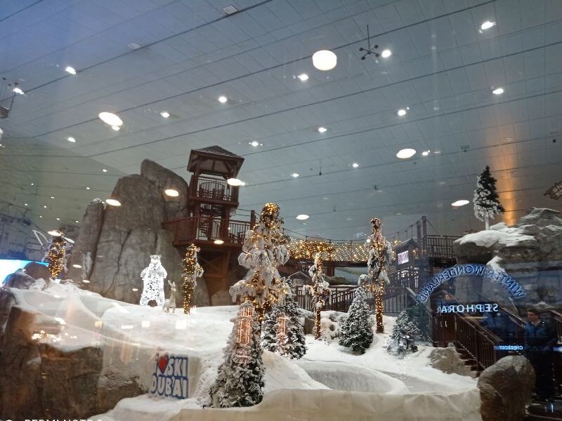 Ski Dubai in the Mall of the Emirates, Dubai Ski Dubai, indoor ski slope at Mall of the Emirates with snow, decorated Christmas trees with lights, wooden buildings, and ski equipment visible.