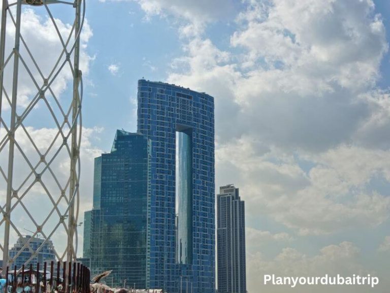 Address Beach Resort at JBR Dubai, a tall blue glass building with a unique opening near the top, shown against a cloudy sky.