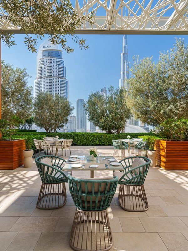 Outdoor restaurant terrace at Address Dubai Mall hotel with tables, olive trees, and views of Burj Khalifa and the Dubai skyline.