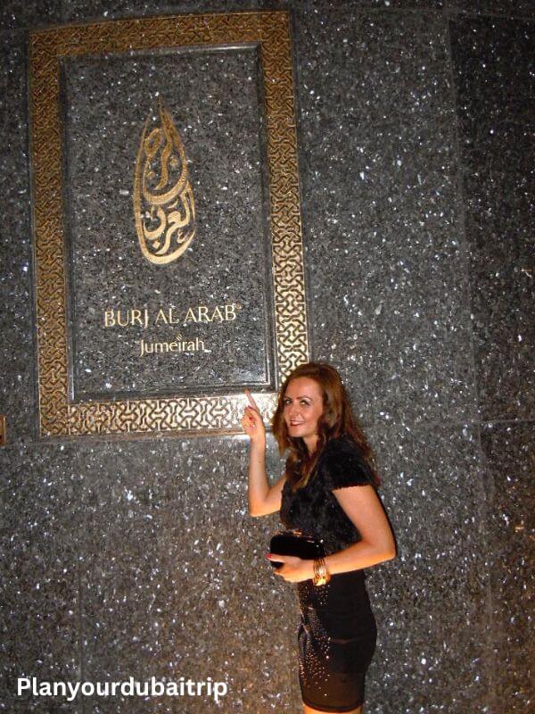 Burj Al Arab sign Woman posing next to the Burj Al Arab Jumeirah sign on a sparkly wall inside the hotel.