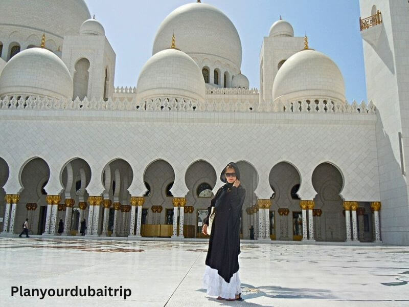 Dress code in Sheikh Zayed Grand Mosque, Abu Dhabi Woman in traditional dress standing in the courtyard of Sheikh Zayed Grand Mosque in Abu Dhabi with white domes and arches in the background.