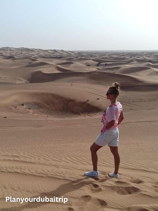 Woman standing on a sand dune in the Dubai desert with rolling dunes stretching out behind her.