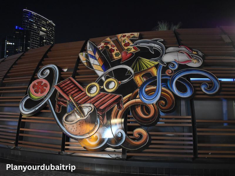Graffiti on building in JBR Dubai Colorful graffiti mural on a building in JBR Dubai showing musical instruments, food, and other objects painted on wooden panels at night.