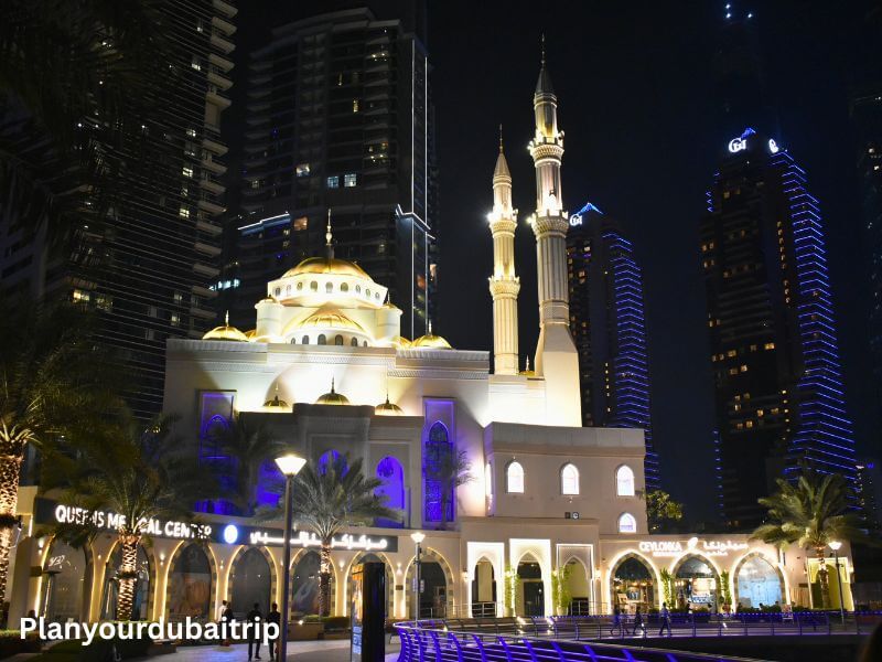 Mohammed Bin Ahmed Al Mulla Mosque in Dubai Marina Mohammed Bin Ahmed Al Mulla Mosque lit up at night in Dubai Marina with white walls, golden domes, and tall minarets surrounded by modern high-rise buildings.