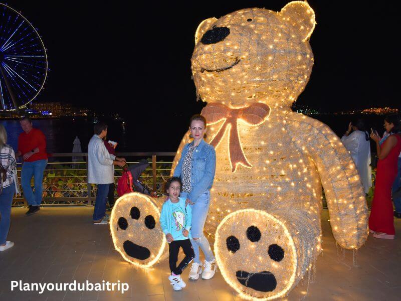 Picture with a bear at JBR Dubai Woman and child posing with a large teddy bear decoration covered in lights at JBR Dubai with the beach and Ain Dubai visible in the background.