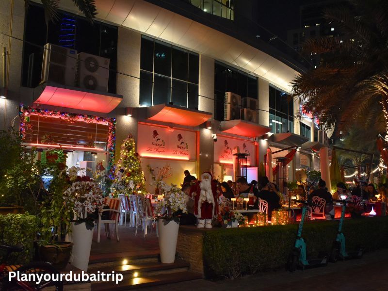 Restaurant in Dubai Marina Outdoor restaurant at Dubai Marina lit up at night with red awnings, diners seated at tables, and colorful flowers decorating the entrance.