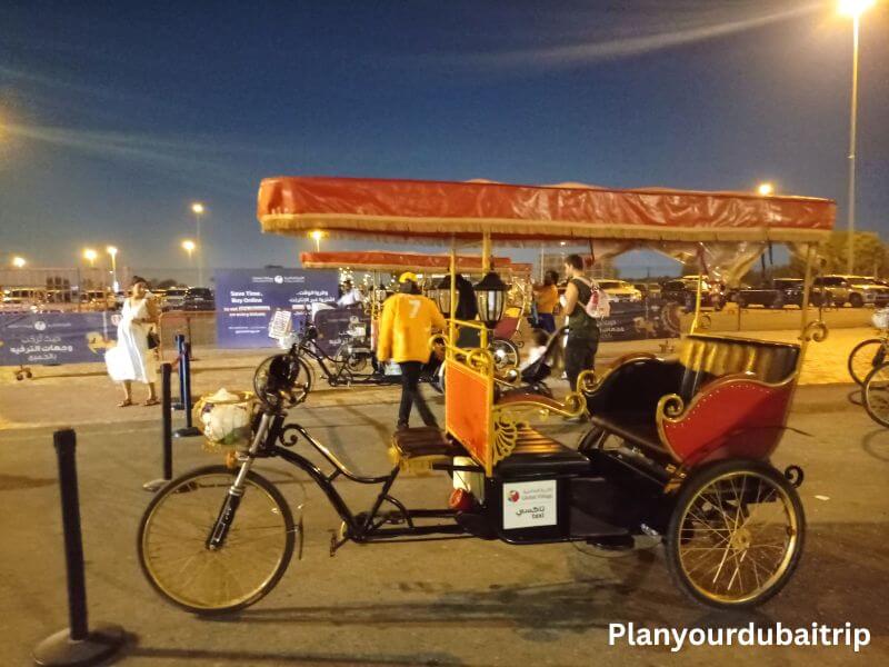 Rickshaw in Dubai Global Village Colorful rickshaw with an orange canopy parked in the lot at Dubai Global Village with people walking around in the evening.