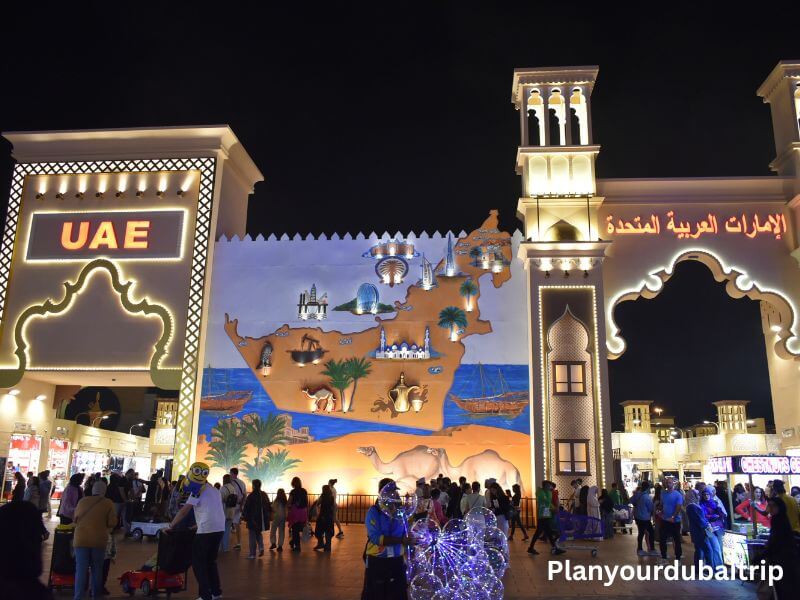 UAE Pavilion in Dubai Global Village UAE pavilion at Dubai Global Village with a large mural showing a map of the Emirates and people walking around in front at night.
