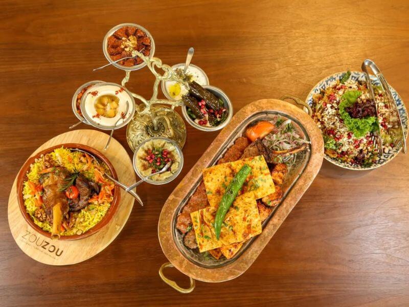 Food spread at Zou Zou Restaurant in Dubai Mall with Middle Eastern dishes including rice with meat, grilled vegetables, salads, and small mezze plates on a wooden table.