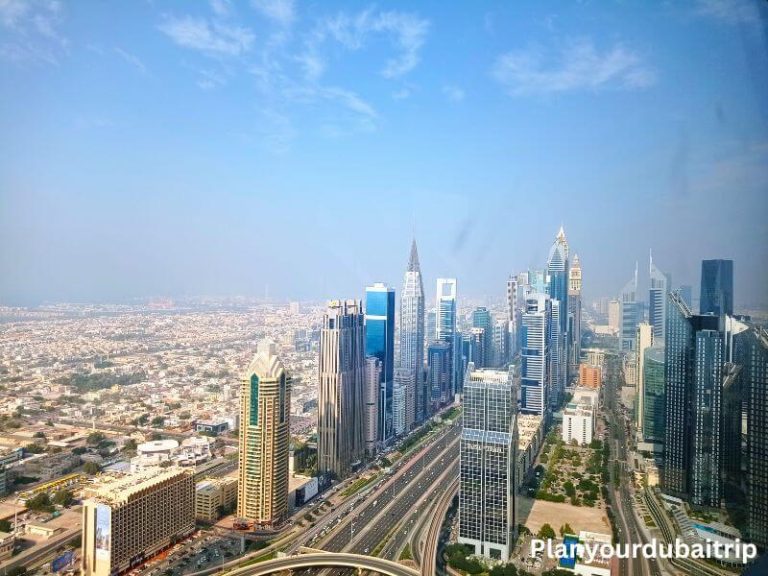 A bird's eye view of Dubai's skyline and Sheikh Zayed Road from Sky Views Dubai, showing tall glass buildings, a busy highway, and the city stretching out into the distance.