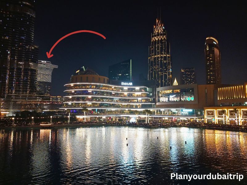 Downtown Dubai pointing to Address Sky View Hotel A night view of Downtown Dubai across the fountain lake, with a red arrow pointing to the Address Sky View Hotel where the Sky Views Observatory is located, surrounded by lit up buildings and the Dubai Mall waterfront.